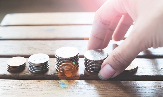 Hand stacking coins in increasing piles on a wooden surface, symbolizing savings or financial growth.
