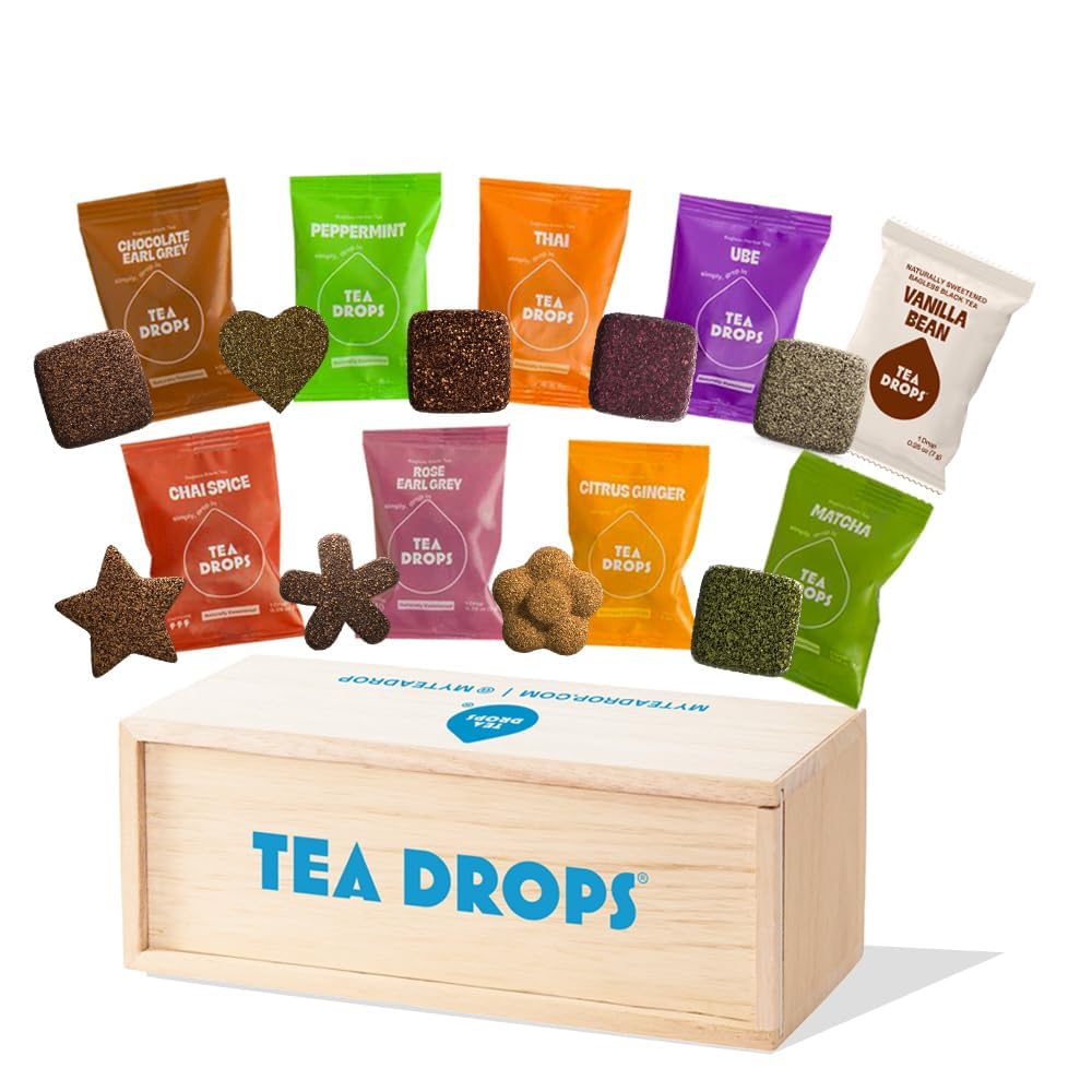 Tea Drops assorted flavored tea tablets in individual colorful packets including Chocolate Earl Grey, Peppermint, Thai, Ube, Vanilla Bean, Chai Spice, Rose Earl Grey, Citrus Ginger, and Matcha, displayed above a wooden Tea Drops gift box.