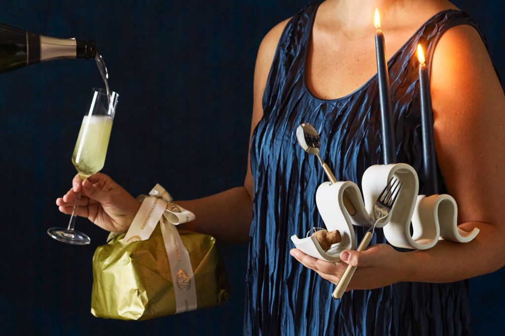 Woman in a blue dress holding a champagne flute being filled and elegant party accessories including candles, ceramic mugs and gold cutlery, capturing a luxurious birthday celebration atmosphere