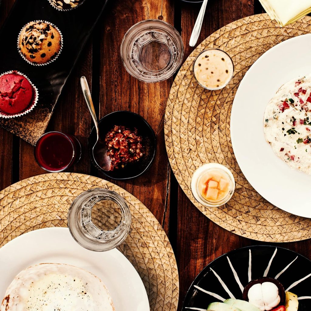 Overhead view of a rustic birthday dinner table spread with cupcakes, dips, sauces and plated dishes on woven placemats, perfect inspiration for a cozy home birthday party food setup.