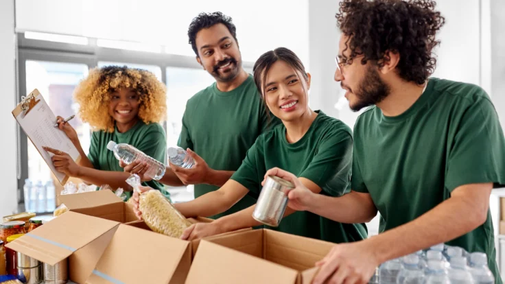 Group of volunteers packing food and water donations into cardboard boxes indoors