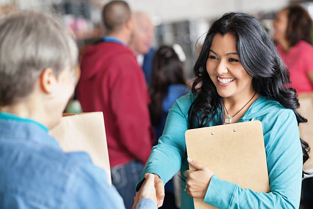 Smiling woman holding a clipboard and shaking hands with another person at a community event.